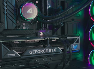 The image depicts the inside of a computer case featuring a high-performance graphics card labeled 'GEFORCE RTX' with RGB lighting. The cooling fans are illuminated with vibrant colors, creating a visually striking look. Various cables and components are neatly arranged, highlighting advanced hardware and a focus on aesthetics.